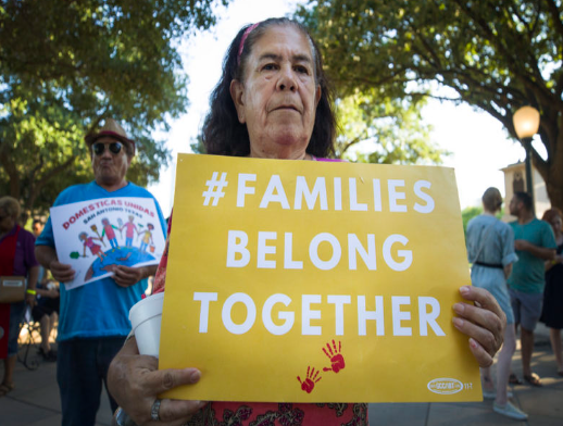 This image shows woman holding sign that reads, “# Families belong together”.